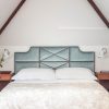 An upholstered headboard in light blue silk velvet with decorative nailings in a white, modern bedroom - Beaumont & Fletcher