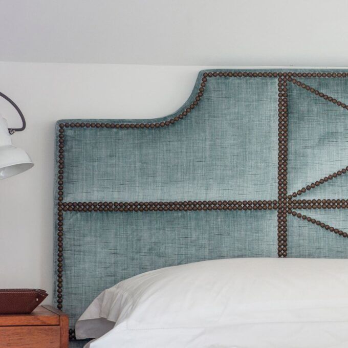 A bespoke headboard upholstered in a pale blue silk velvet with decorative nailings