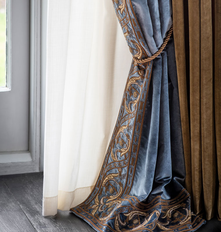 Blue curtain with gold embroidery. White curtain behind. Black wooden floor.