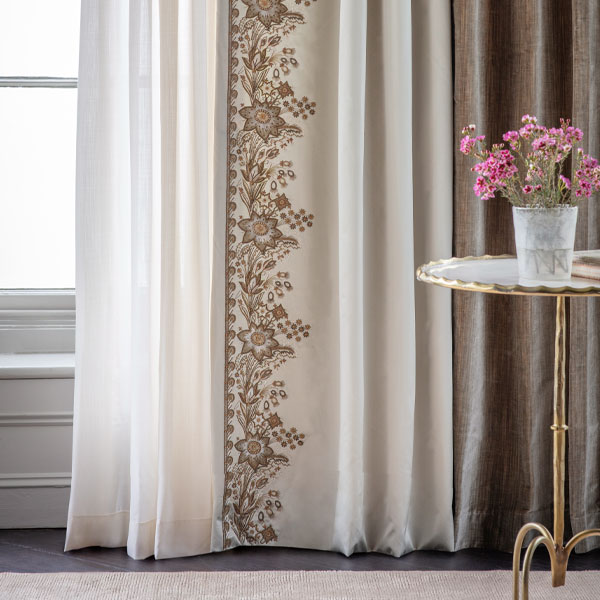 White curtain with gold embroidery. Table with plant pot, pink flowers